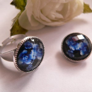 Könnte beinhalten: Ein silberner Ring und ein Knopf mit einem blauen und weißen Blumendesign auf schwarzem Hintergrund.
