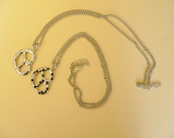 May include: Two silver necklaces with pretzel-shaped pendants. Each pendant is decorated with black stones.