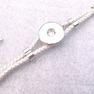 Può includere: Braccialetto in pelle bianca con un bottone a pressione argentato e una chiusura argentata. Il braccialetto è intrecciato e ha una catena argentata attaccata alla chiusura.