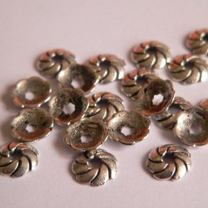 Può includere: Un gruppo di cappucci per perline in metallo argentato con un design a spirale. I cappucci hanno un diametro di circa 1 cm e hanno un foro al centro.