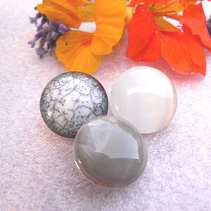 Può includere: Tre cabochon rotondi in vetro, uno con un motivo craquelé bianco e nero, uno bianco e uno grigio.