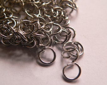 May include: A pile of silver jump rings, a type of jewelry finding used for connecting chains, cords, and other jewelry components.