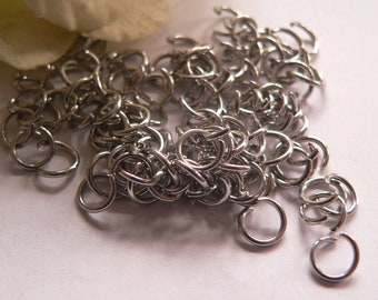 May include: A pile of silver jump rings, a type of jewelry finding used for connecting chains, cords, and other jewelry components.