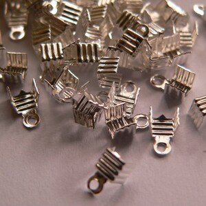 Può includere: Un mucchio di chiusure in metallo argentato per la creazione di gioielli. Le chiusure sono piccole e hanno un design semplice.