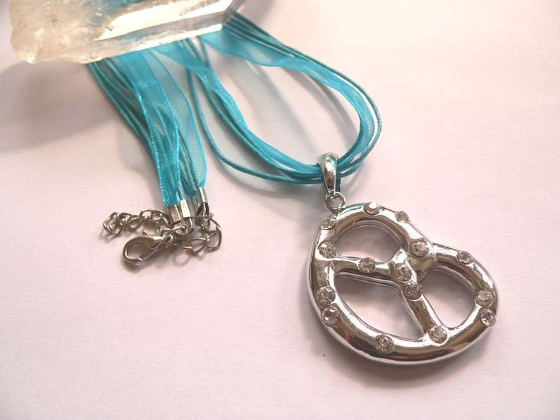 Peut inclure: Un collier avec un pendentif en forme de bretzel argent&eacute; orn&eacute; de strass transparents, suspendu &agrave; un ruban bleu turquoise.