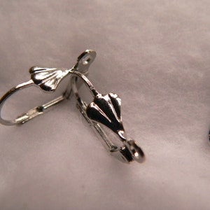 Peut inclure: Deux fermoirs d'oreille en argent avec un motif en forme d'éventail décoratif. Les fermoirs sont ouverts et prêts à être fixés aux boucles d'oreilles.