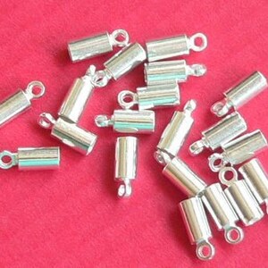 Può includere: Un gruppo di tappi terminali in metallo argentato per la creazione di gioielli. I tappi terminali sono cilindrici con un piccolo anello ad un'estremità.