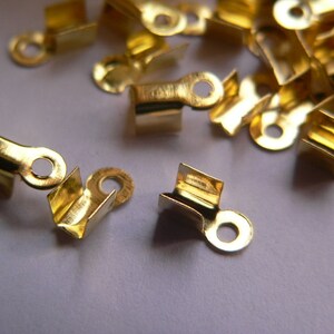 Könnte beinhalten: Ein Haufen goldfarbener Metallverschlüsse mit einer kleinen Schlaufe an jedem. Die Verschlüsse sind zum Befestigen von Stoff oder anderen Materialien gedacht.