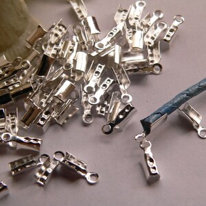 Può includere: Un mucchio di chiusure in metallo argentato per la creazione di gioielli. Le chiusure hanno un anello a un'estremità e un piccolo pezzo piatto all'altra estremità. Sono progettate per essere utilizzate con cordoncino o pelle.