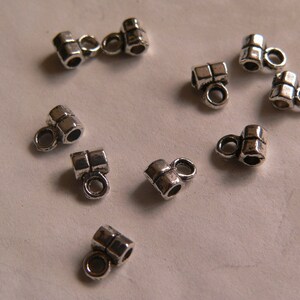 Op de afbeelding: Tien zilverkleurige metalen kralencaps met elk twee gaten. De caps zijn ontworpen om te worden gebruikt als eindkappen voor kettingen, armbanden of andere sieradenprojecten.