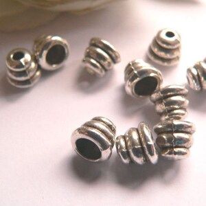 Può includere: Cappucci per perline in metallo argentato con un design rigato. I cappucci hanno un diametro di circa 1 cm e un foro al centro per infilare.
