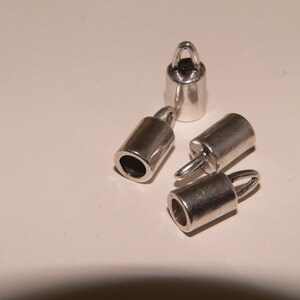 Può includere: Quattro tappi terminali in metallo argentato con un anello nella parte superiore. I tappi terminali sono cilindrici e hanno una finitura liscia.