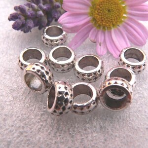 Peut inclure: Gros plan sur dix perles d'espacement en métal argenté avec un motif diamanté texturé. Les perles sont disposées en cercle sur une surface blanche.