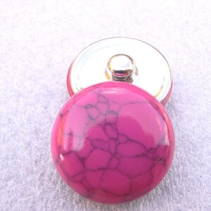 Könnte beinhalten: Ein pinkfarbener und weiß gemusterter Druckknopf mit silberner Metallrückseite.