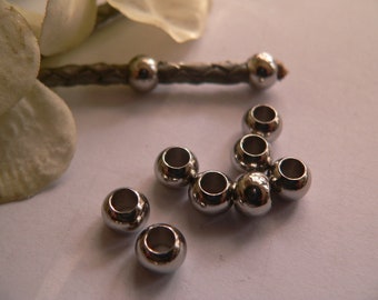 May include: A close-up of ten silver metal beads with a hole in the center. The beads are arranged in a semi-circle on a white surface.