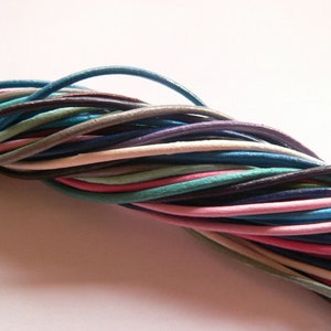 Peut inclure: Un assortiment de cordons en cuir de différentes couleurs, notamment du bleu, du rose, du vert, du blanc et du marron. Les cordons sont entrelacés et disposés de manière aléatoire.