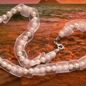 May include: A white pearl necklace with a white ribbon. The necklace is on a brown surface.