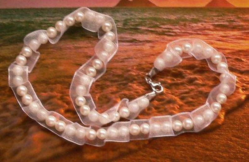 May include: A white pearl necklace with a white ribbon. The necklace is on a brown surface.