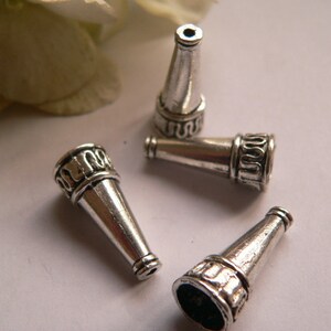 Può includere: Quattro tappi per perline in metallo argentato a forma di cono con dettagli decorativi. I tappi sono progettati per essere utilizzati come tappi finali per collane, braccialetti o altri progetti di gioielleria.