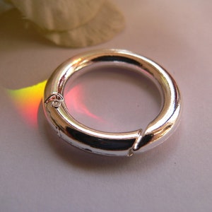 Könnte beinhalten: Ein silberner Ring mit einem kleinen, klaren Stein in der Mitte. Der Ring ist offen und hat eine glatte, polierte Oberfläche.