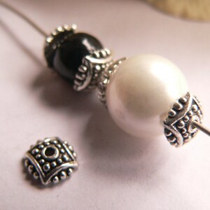 Può includere: Primo piano di una collana di perline argentate e nere con una perla bianca. La collana è realizzata con perline distanziatrici argentate e una chiusura argentata.
