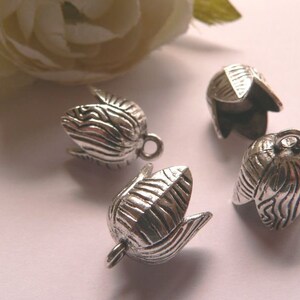Può includere: Quattro cappucci pendenti in metallo argentato a forma di fiore con una superficie testurizzata. I cappucci hanno un anello nella parte superiore per il fissaggio a un cordino o una catena.