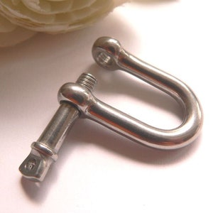 Könnte beinhalten: Ein silberner Schraubverschluss mit einem D-Ring. Der Verschluss ist aus Edelstahl und hat eine polierte Oberfläche.