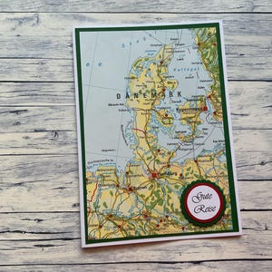 Könnte beinhalten: Eine grün-weiße Karte mit einer Karte von Dänemark und dem Text "Gute Reise" in einem roten Kreis.