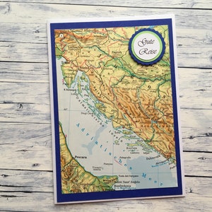 Könnte beinhalten: Eine blaue und weiße Karte mit einer Karte von Kroatien und dem Text "Gute Reise" in einem grünen und blauen Kreis.