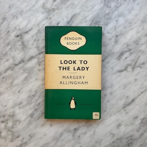 May include: A vintage paperback book titled "Look to the Lady" by Margery Allingham. The book has a green cover with a cream-colored band across the middle. The Penguin Books logo and a penguin illustration are visible.