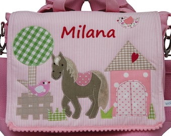 May include: Pink children's backpack featuring a horse, a bird, a tree, and a house design. The backpack is made from pink and white striped fabric with a white trim. The name "Milana" is embroidered on the front of the backpack.