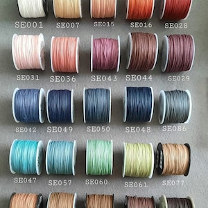 Könnte beinhalten: Eine Sammlung von 18 Spulen gewachster Baumwollschnur in verschiedenen Farben, darunter Weiß, Beige, Rosa, Rot, Braun, Lila, Blau, Grün und Grau. Jede Spule ist mit einem Code gekennzeichnet, wie z. B. "SE001", "SE007", "SE015" usw.