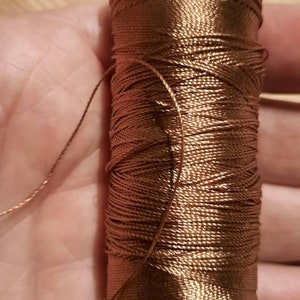 May include: A spool of brown thread with a shiny finish.