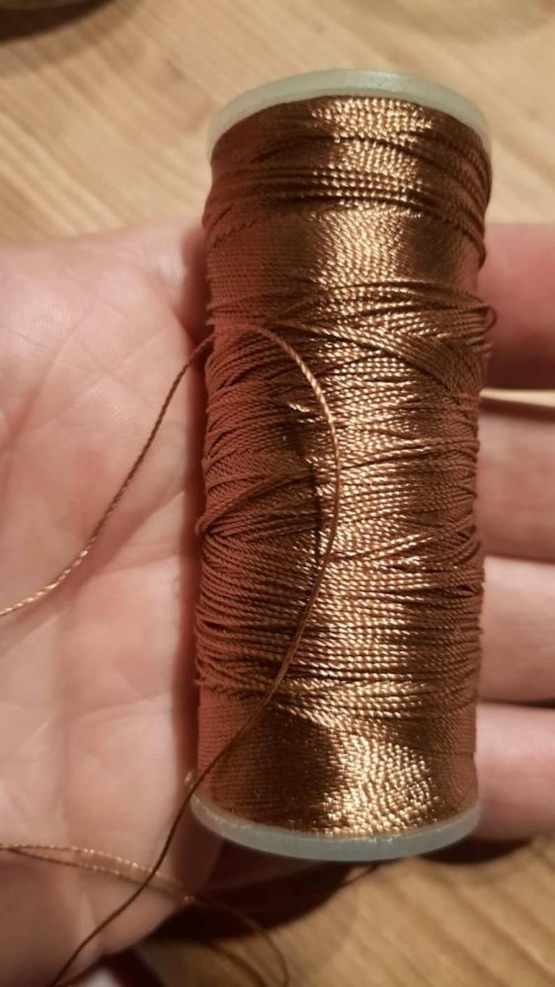 May include: A spool of brown thread with a shiny finish.
