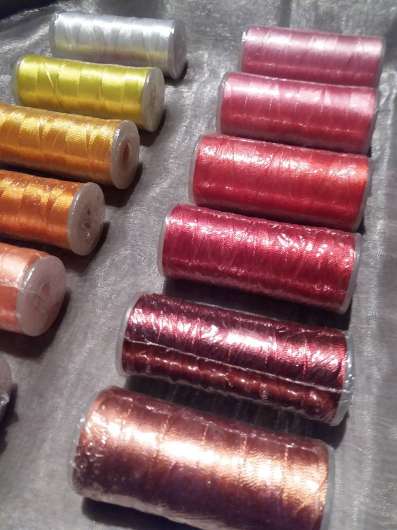 May include: Assortment of spools of thread in various colours, including silver, yellow, orange, red, and brown. The spools are wrapped in clear plastic.