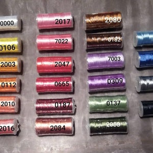 May include: A collection of 20 spools of thread in various colours, including white, yellow, orange, red, pink, purple, blue, green, and black. Each spool is labelled with a number.