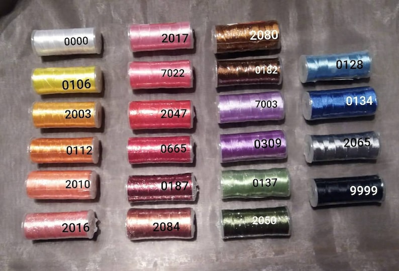 May include: A collection of 20 spools of thread in various colours, including white, yellow, orange, red, pink, purple, blue, green, and black. Each spool is labelled with a number.