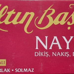 May include: A red box with gold lettering that reads "Altın Başak" and "NAYLON" with the text "DİKİŞ, NAKİŞ, DANTEL İPLİĞİ" below. The box also has the text "&Ccedil;IKMAZ BOYALI" and "SAĞLAM &bull; PARLAK &bull; SOLMAZ" on it.