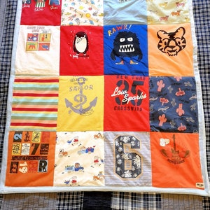 May include: A patchwork quilt made from a variety of t-shirts. The quilt is made up of 12 squares, each with a different design. The designs include a penguin, a monster, a tiger, a sailboat, a number 6, a guitar, and more. The quilt is a great way to reuse old t-shirts and create a unique and personal piece of art.
