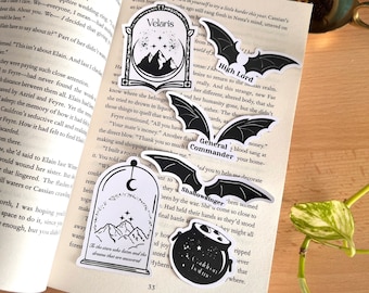 Puede incluir: Cinco pegatinas en blanco y negro con ilustraciones de montañas, una luna creciente, estrellas y un caldero. Las pegatinas tienen texto que dice "Velaris", "High Lord", "General Commander", "Shadowsinger" y "Cauldron Inside".