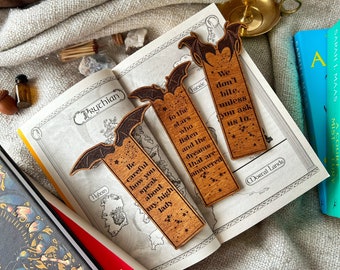 May include: Two wooden bat bookmarks with engraved sayings. The first bookmark says "Be careful how you speak about my high lady." The second bookmark says "To the stars who listen and the dreams that are answered. We don't bite, unless you ask us to."