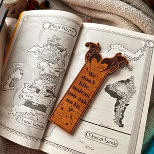 May include: Wooden bookmark featuring a dragon with wings outstretched and the text "We don't bite, unless you ask us to."