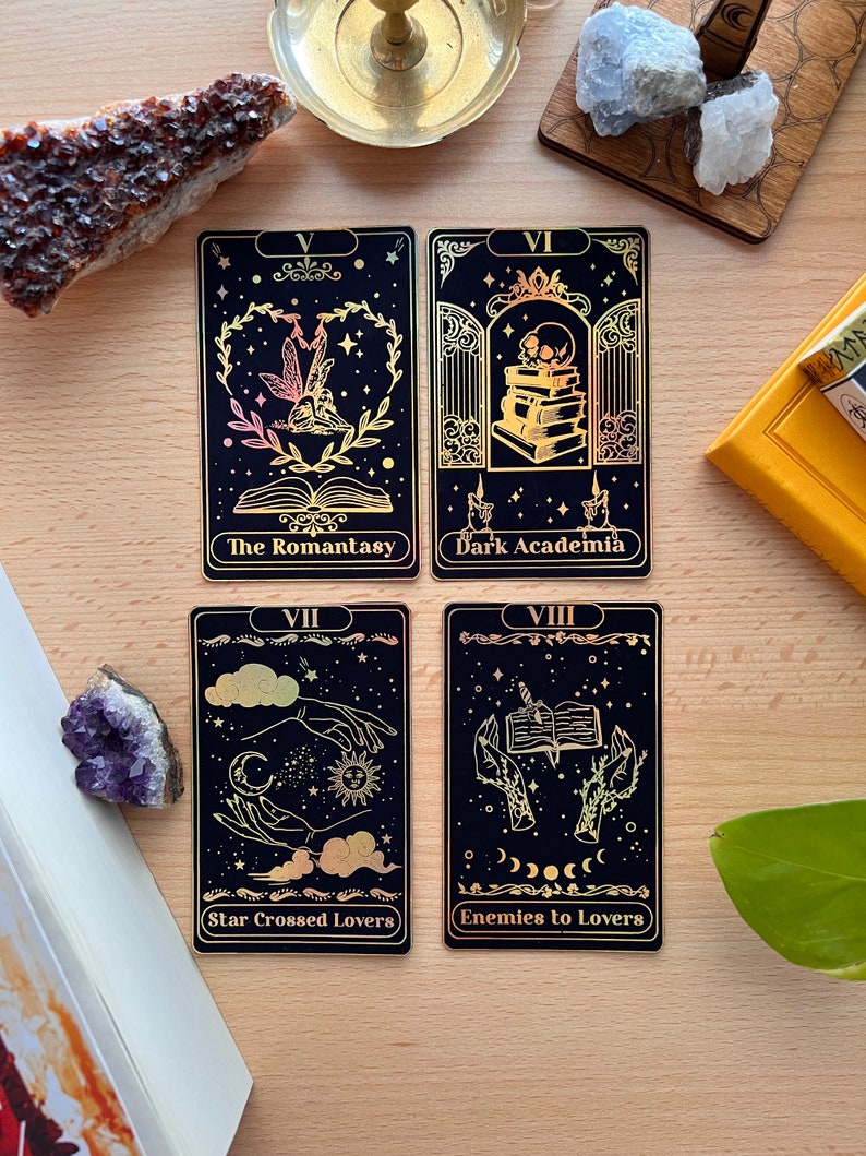 May include: Four black tarot cards with gold foil accents and illustrations. The cards are titled "The Romantasy", "Dark Academia", "Star Crossed Lovers", and "Enemies to Lovers".