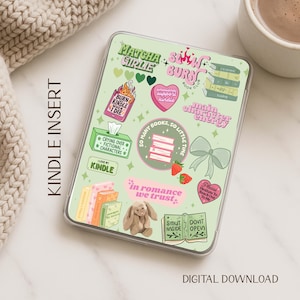 May include: A light green Kindle insert with various stickers. Stickers include text like "Matcha Girlie", "Burn Kindle When I Die", and "In Romance We Trust". A small stuffed bunny and a stack of books are also visible.