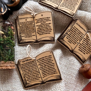 May include: A set of three wooden book ornaments with engraved text from the Harry Potter series. The ornaments are shaped like open books with brown covers and white text. The text on the ornaments reads "The Boy Who Lived", "The Tributes", and "An Unexpected Party".