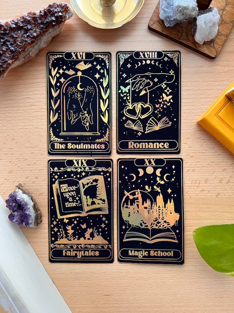 May include: Four tarot cards with gold foil accents on a black background. The cards are numbered XVI, XVIII, XIX, and XX. The card titles are "The Soulmates", "Romance", "Fairytales", and "Magic School".