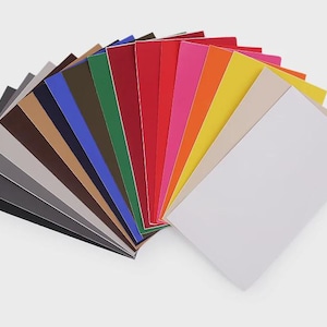 Könnte beinhalten: Ein Fächer aus farbigem Kartonpapier in verschiedenen Farbtönen. Die Farben umfassen Schwarz, Grau, Braun, Blau, Grün, Rot, Rosa, Orange, Gelb und Weiß. Die Papiere sind in einem halbkreisförmigen Muster angeordnet.