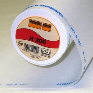 Peut inclure: Un rouleau de tissu d'entoilage blanc étiqueté "Vlieseline H 200" avec le texte "viieseline vilene" et "90 cm x 25 m 100% PES".
