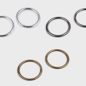 Könnte beinhalten: Eine Sammlung von Metallringen in Silber-, Gunmetal- und Messingtönen. Die Ringe sind kreisförmig, mit einer kleinen Lücke im Umfang. Die Ringe werden wahrscheinlich für Bastelarbeiten, Schmuckherstellung oder als Hardware-Komponenten verwendet.
