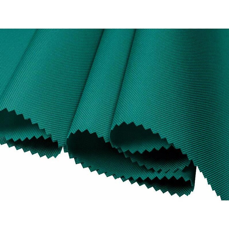 May include: Close-up of a folded section of teal fabric. The fabric has a textured weave and a jagged edge. The folds create shadows and highlights, emphasizing the fabric's texture and color. The fabric is a solid, vibrant teal.